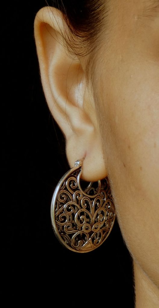 Close-up of a woman wearing a decorative, filigree-style earring that resembles a basket or purse, showcasing intricate swirls and designs.