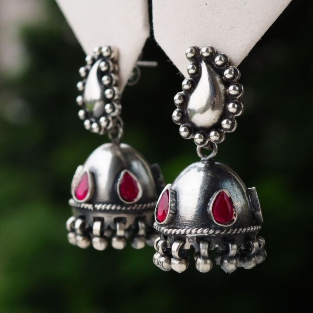 Close-up of traditional silver earrings with red gemstones, showcasing intricate design and detailing.