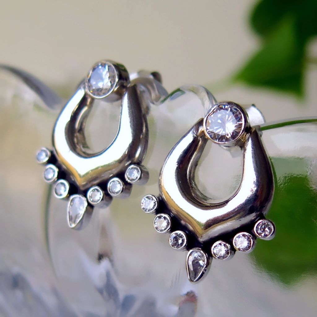 Close-up of elegant silver earrings with multiple sparkling stones, displayed on a glass surface.