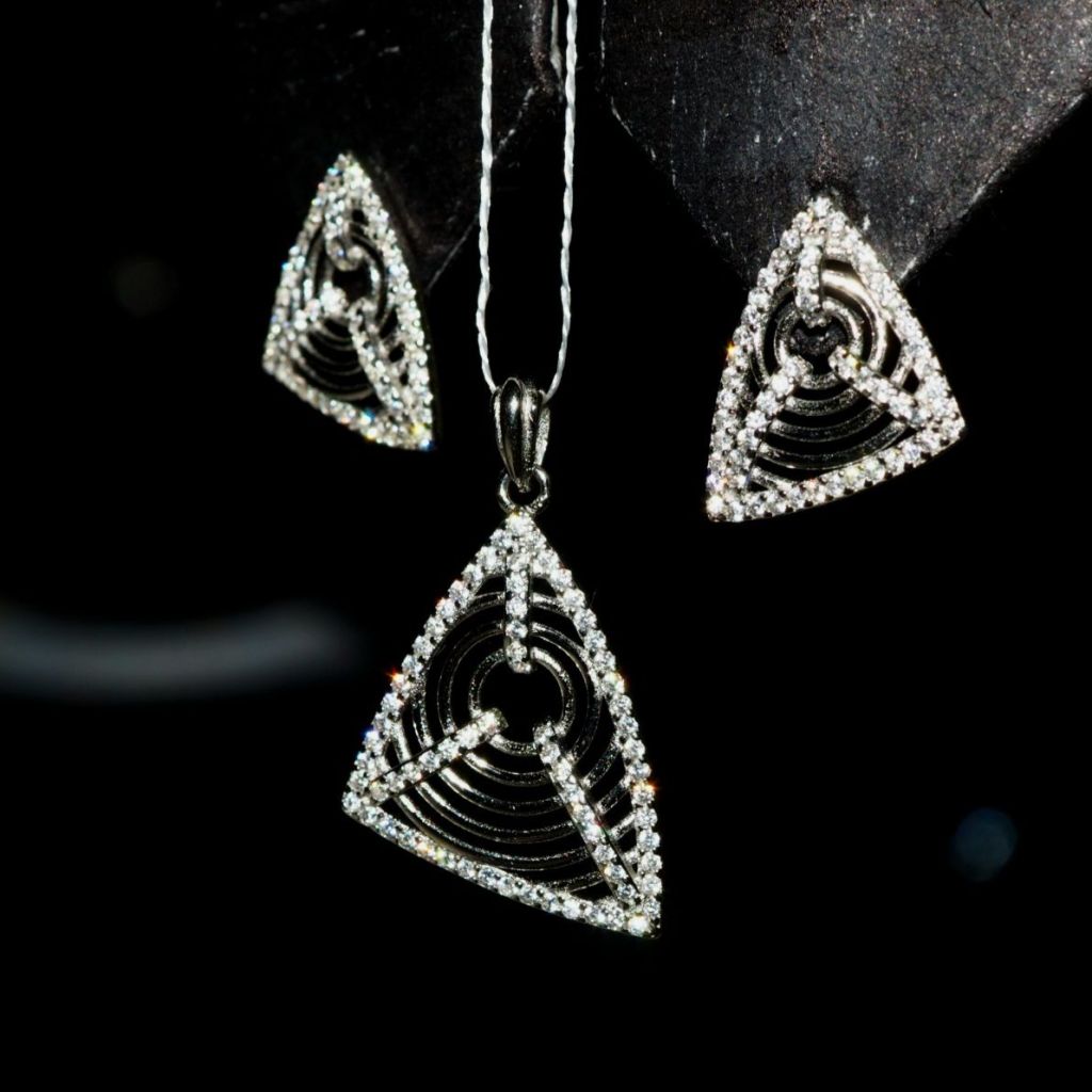 A set of triangular earrings and a pendant crafted in 925 silver adorned with diamond-like cubic zirconia stones, displayed against a dark background.