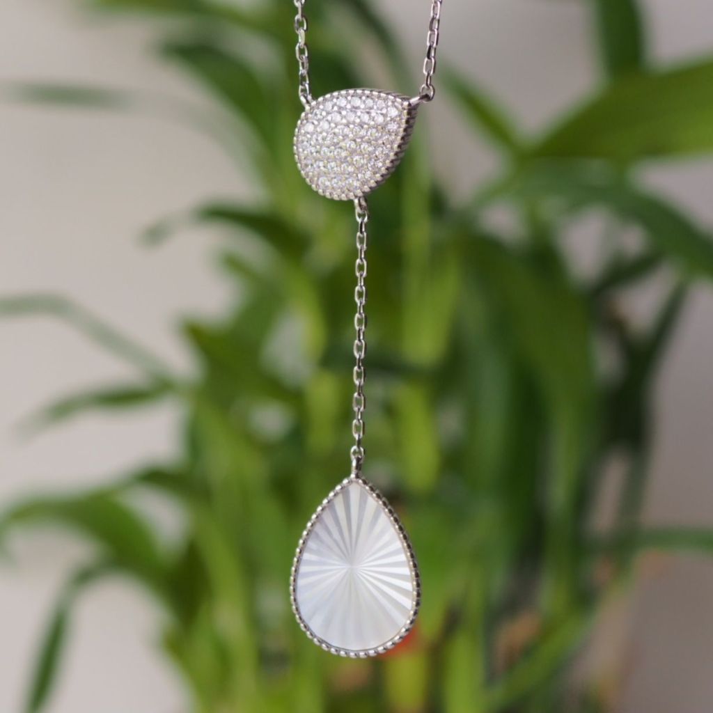Close-up of a pendant featuring a sparkling, teardrop-shaped gemstone with a textured Mother of Pearl design, suspended from a delicate chain.
