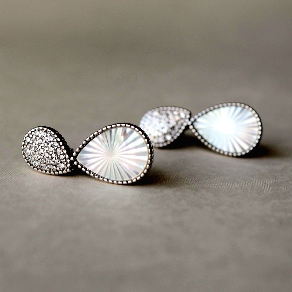 Two earrings featuring crepuscular Mother of Pearl gemstones with intricate silver detailing.