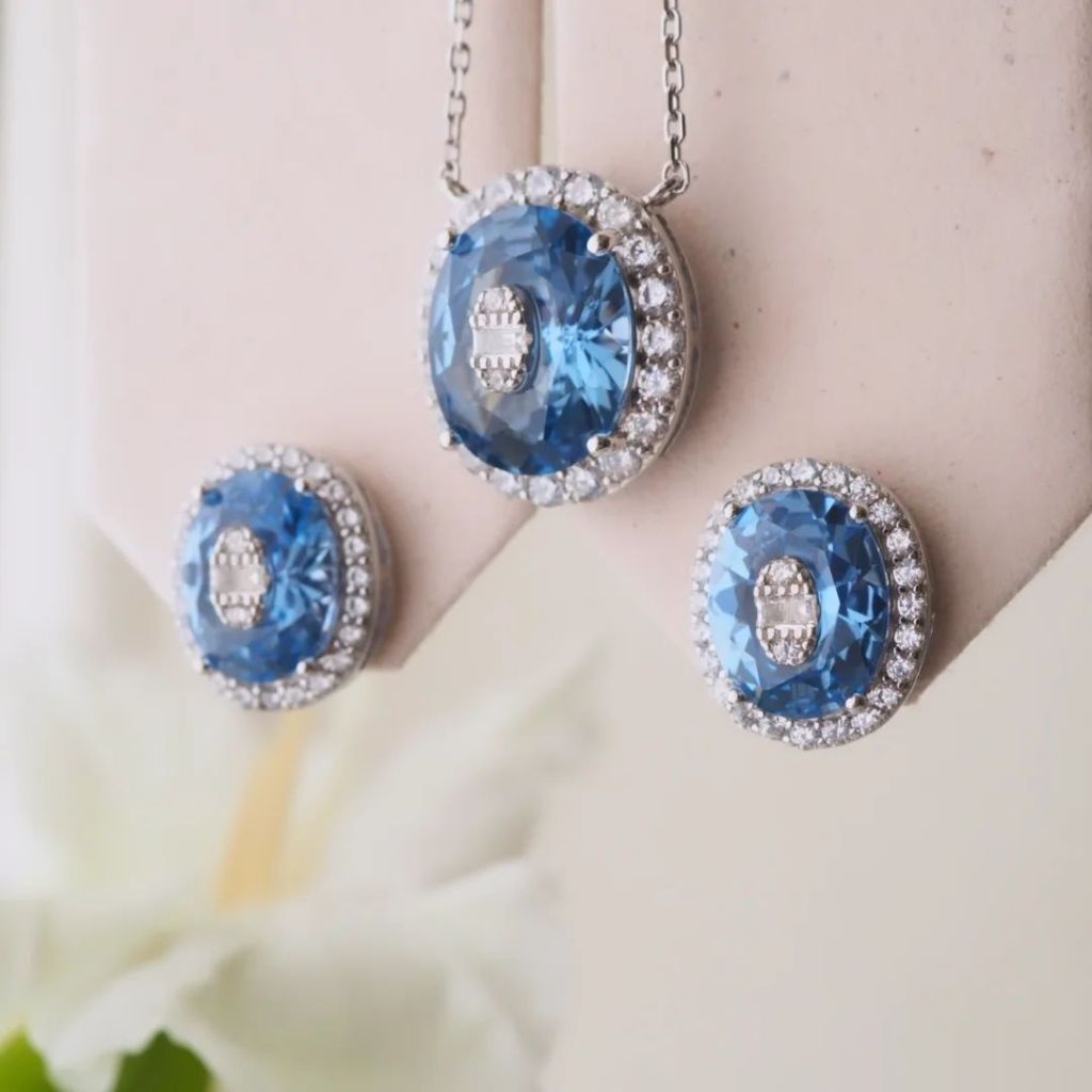 Close-up of elegant jewelry set featuring a pendant and earrings with sparkling Cobalt Blue stones surrounded by shimmering accents.
