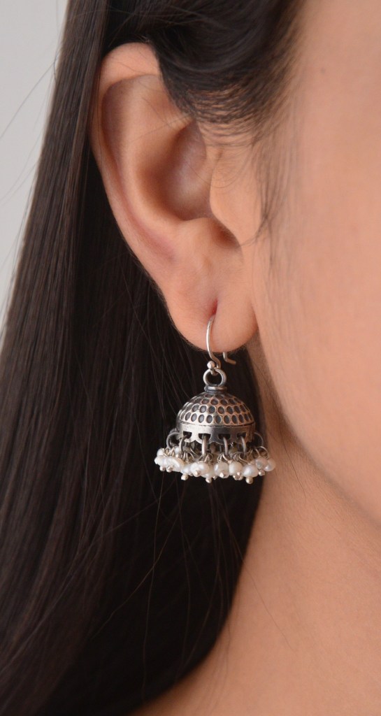 Close-up of a woman wearing a decorative silver jhumki earring with pearl accents.