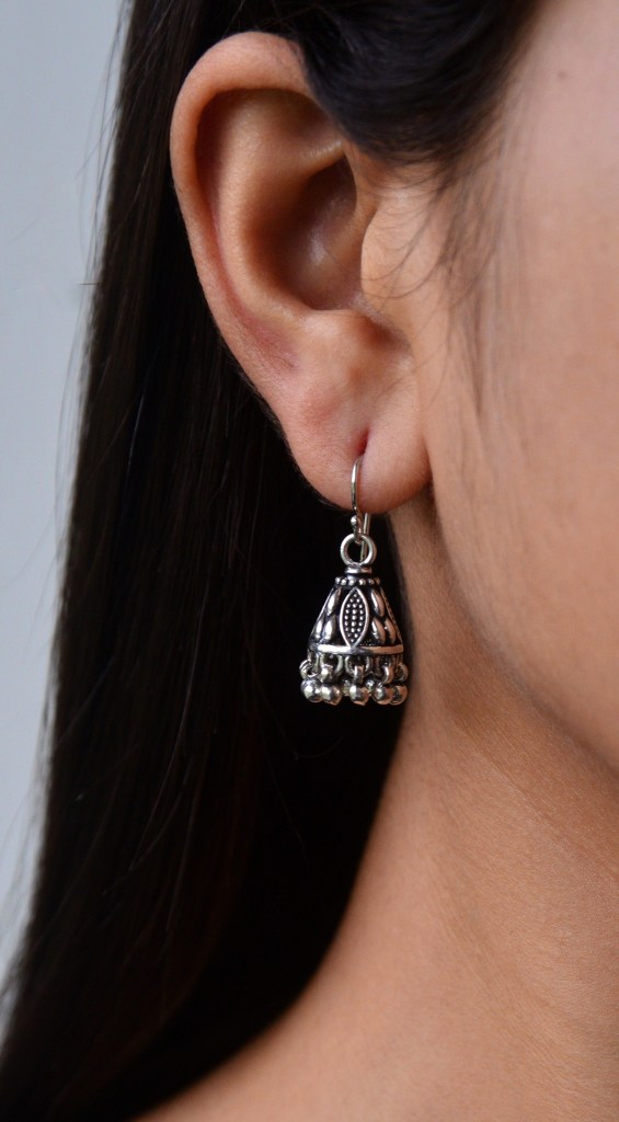 Close-up of a person wearing a silver jhumki earring, showcasing intricate design and detail.
