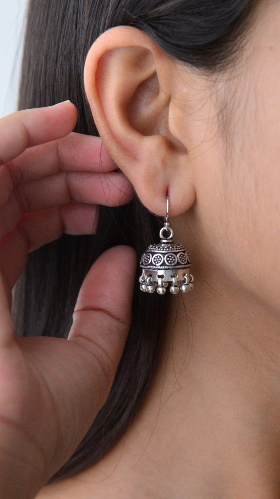 Close-up of a woman wearing a stylish silver jhumka earring, showcasing the intricate design and detail, while her hand gently touches the earring.