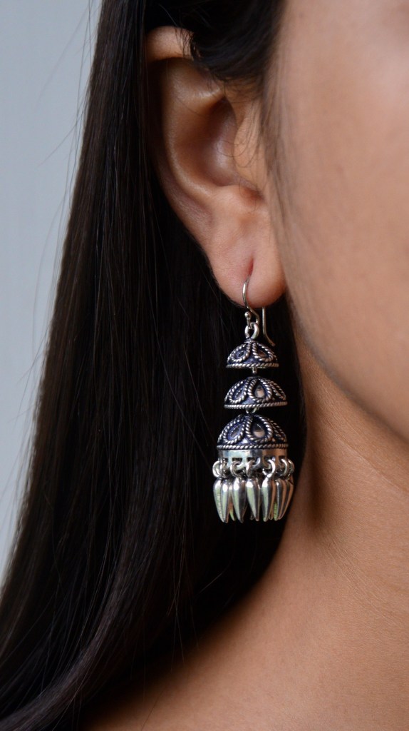 A close-up of a woman's ear adorned with a decorative silver earring featuring intricate designs and dangling elements.