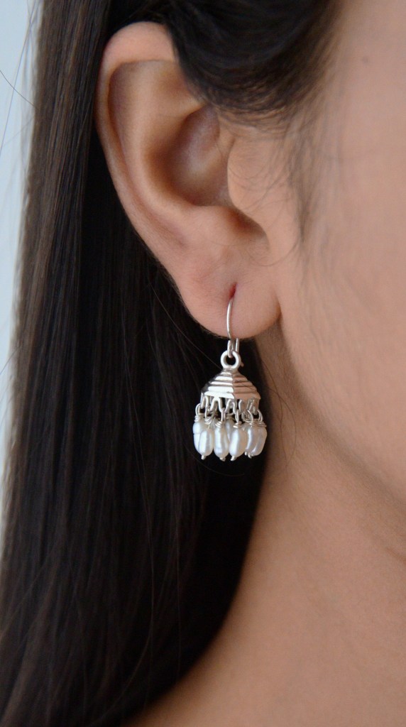 Close-up of a person's ear adorned with a silver chandelier earring featuring white beads.