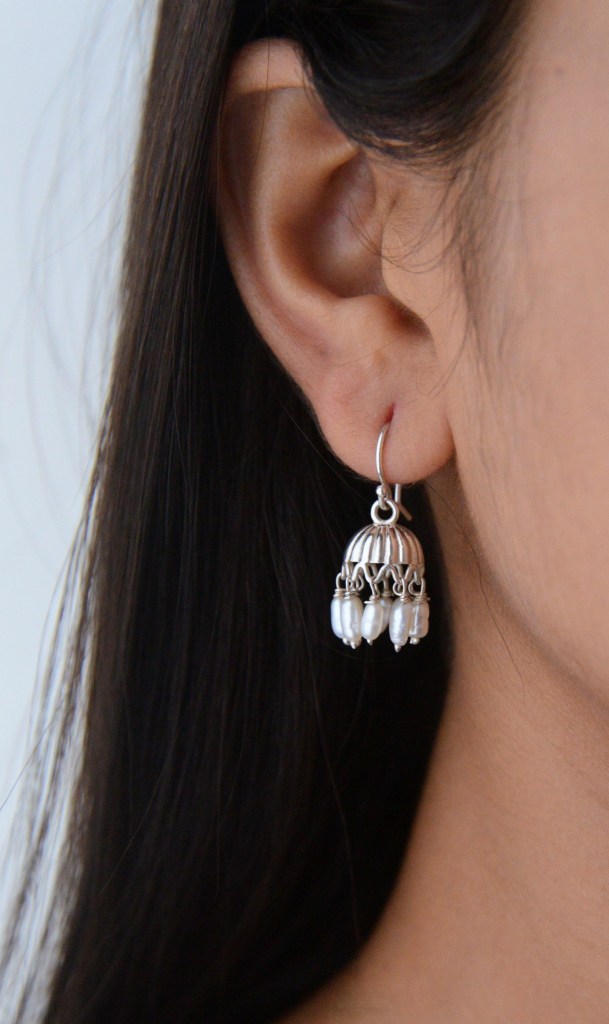 A close-up of a person's ear adorned with a silver chandelier earring featuring decorative elements and pearl-like beads.