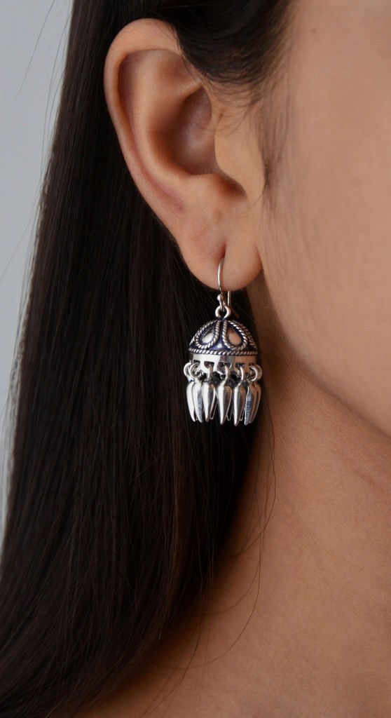 Close-up of a woman's ear wearing a detailed silver earring with a dangle design.