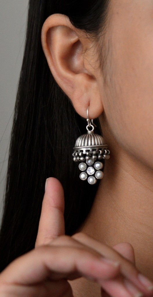 A close-up of a woman wearing a traditional silver earring with intricate detailing, featuring pearls and sparkling stones.
