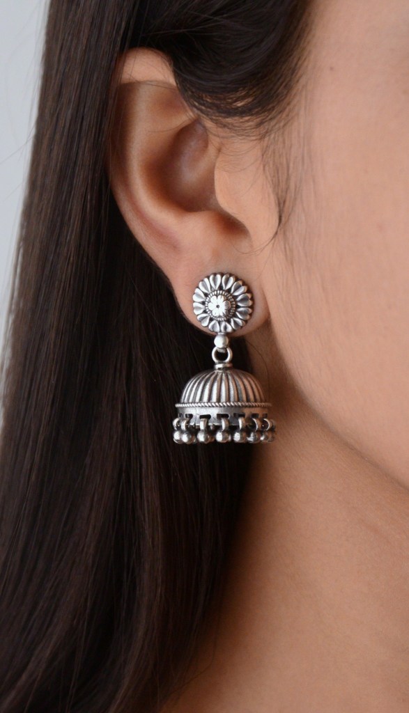 Close-up of a woman wearing silver earrings with a floral design and hanging dome-shaped charms.