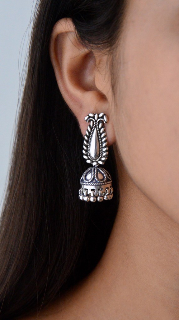 A close-up of a woman wearing intricate silver earrings, showcasing a teardrop design and ornate detailing.