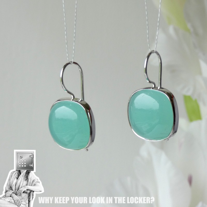 Close-up of a pair of earrings featuring round turquoise stones set in silver hooks, displayed against a neutral background.