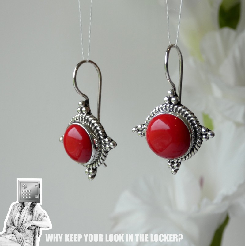 A pair of ornate silver earrings featuring bright red cabochon stones, displayed elegantly against a soft background.