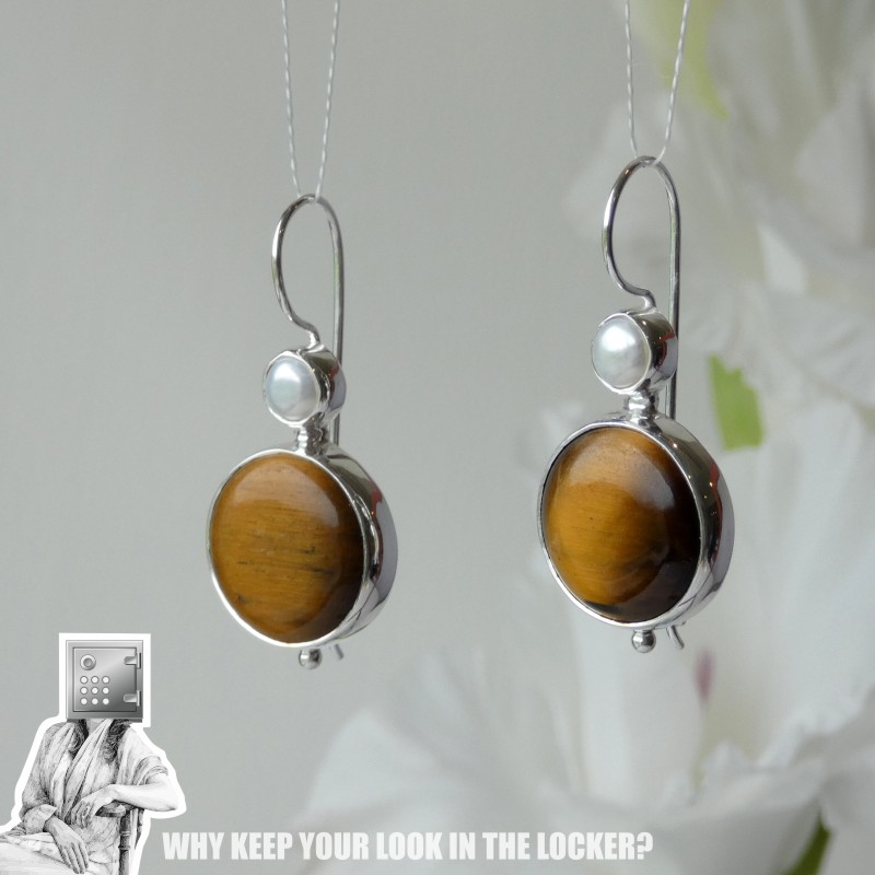 A close-up of silver earrings featuring round tiger's eye stones with a small pearl accent on top.