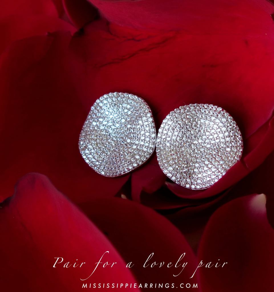 Close-up of a pair of sparkling silver earrings resting on red rose petals.