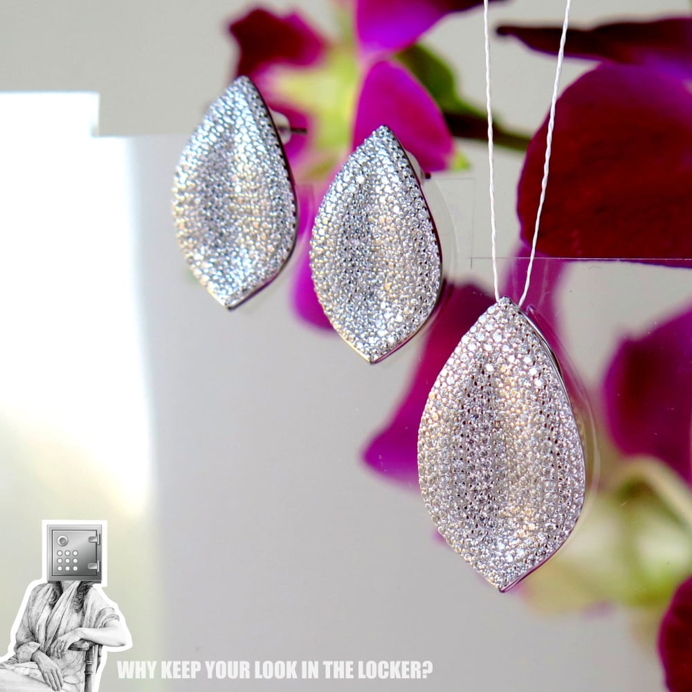 A set of sparkling silver leaf-shaped earrings and a matching pendant displayed against a blurred floral background.