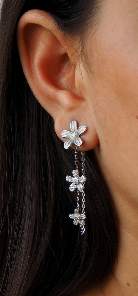 Close-up of a woman's ear featuring stylish silver flower earrings with dangling chains.
