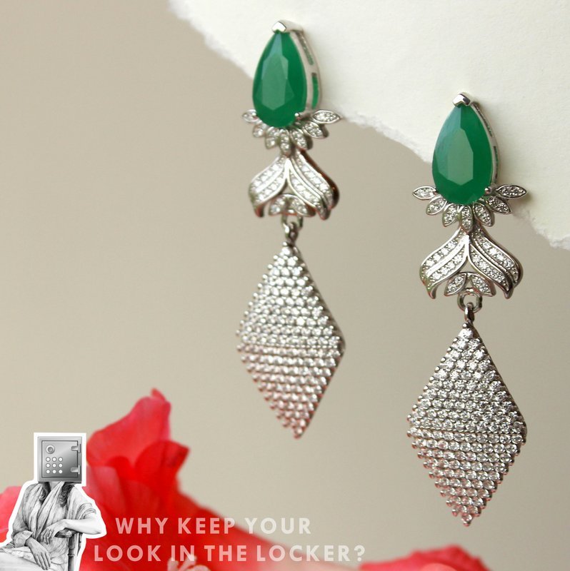 Elegant silver earrings with a teardrop green stone and diamond-like embellishments, featuring a floral design and a long, sparkling pendant.