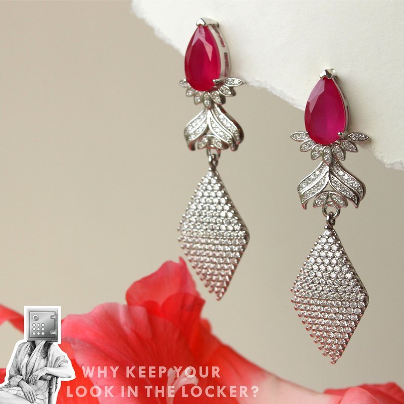 A pair of elegant silver earrings featuring a pear-shaped pink gemstone at the top and a diamond-patterned drop design, set against a soft background with a pink flower.