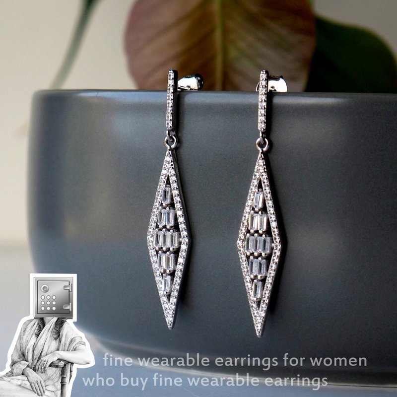 A pair of elegant, diamond-shaped earrings featuring intricate designs and sparkling accents, displayed on a smooth surface with a subtle plant in the background.