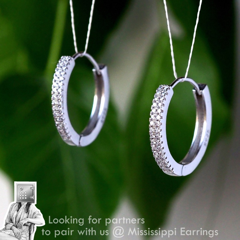 A pair of silver hoop earrings adorned with sparkling rhinestones, displayed against a green background, highlighting their shine and elegance.