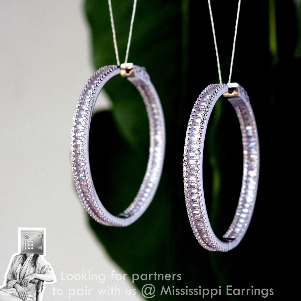 Close-up of sparkling silver hoop earrings with intricate crystal detailing, suspended against a blurred green background.