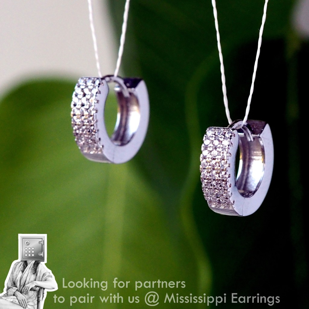 Close-up of shiny silver earrings with sparkling embellishments, displayed against a green background.