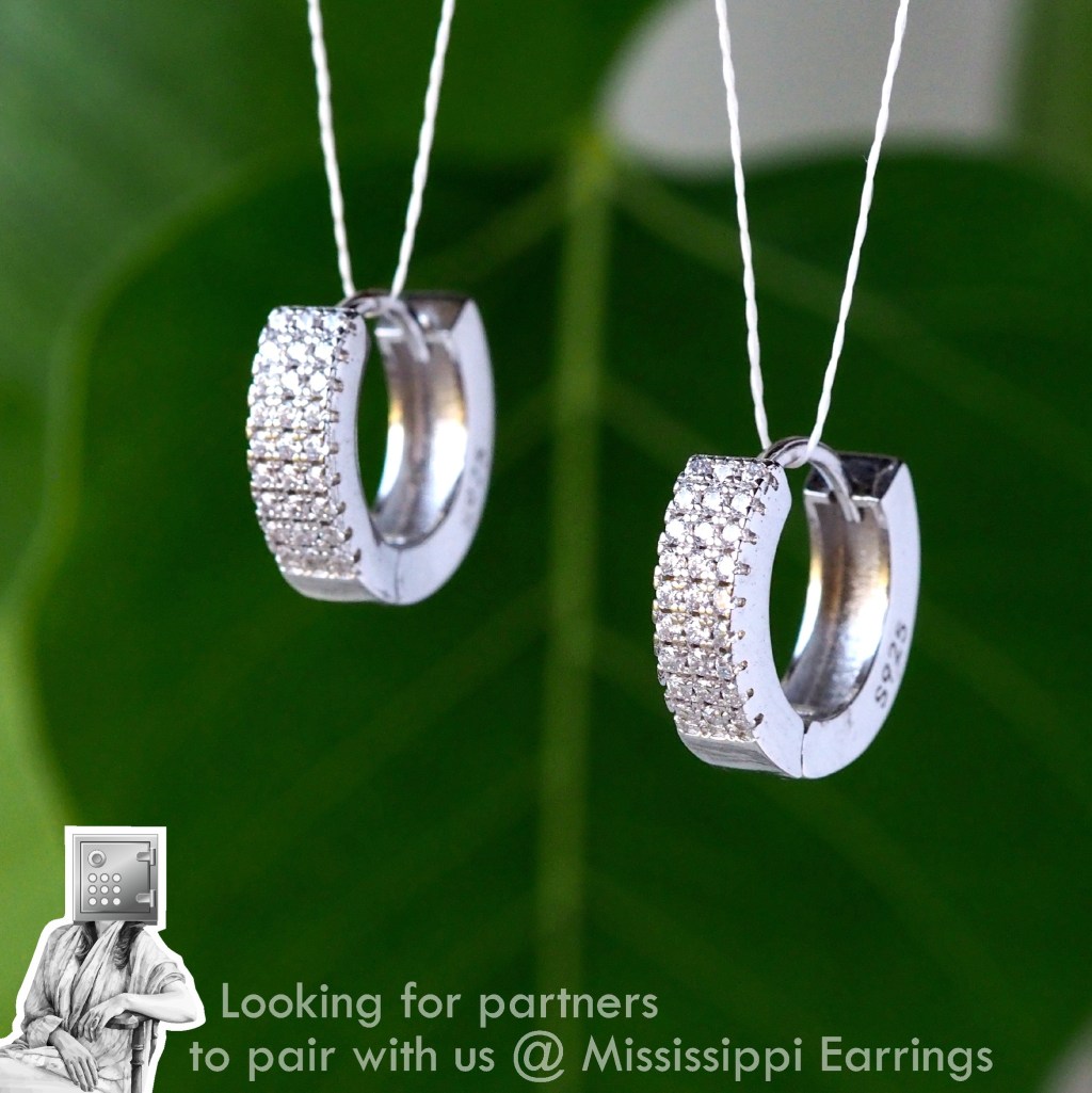Close-up of elegant silver hoop earrings with sparkling embellishments, displayed against a green leafy background.
