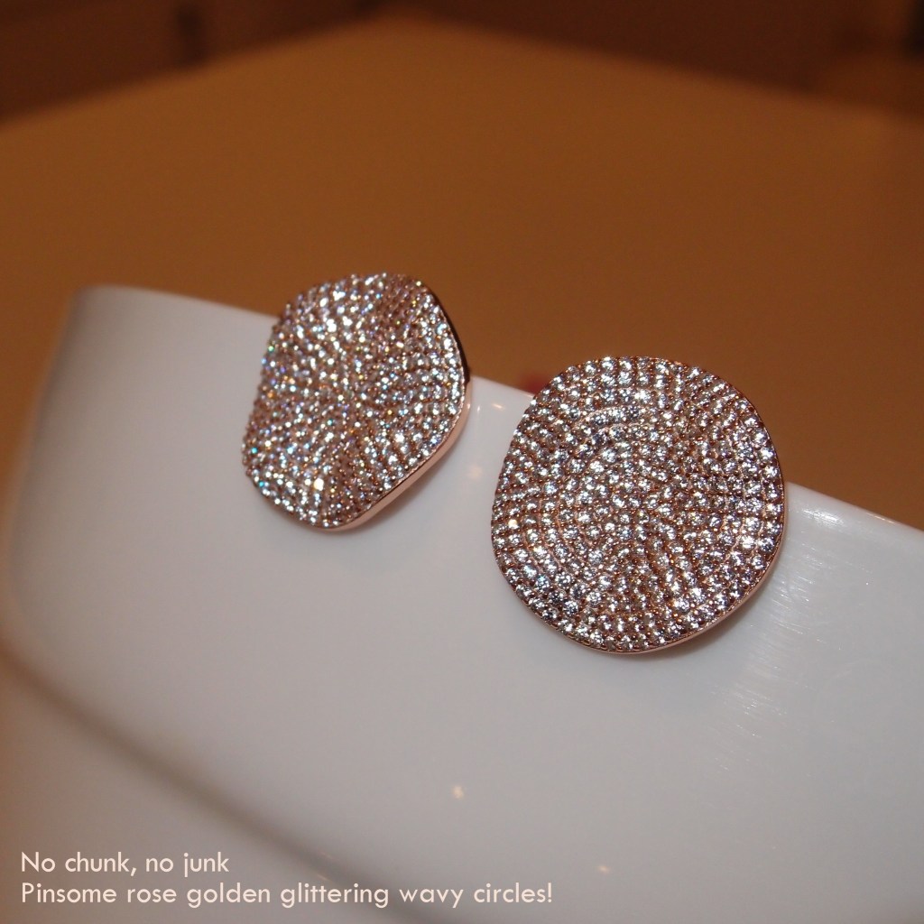 A pair of rose golden earrings featuring glittering wavy circular designs placed on a white surface.
