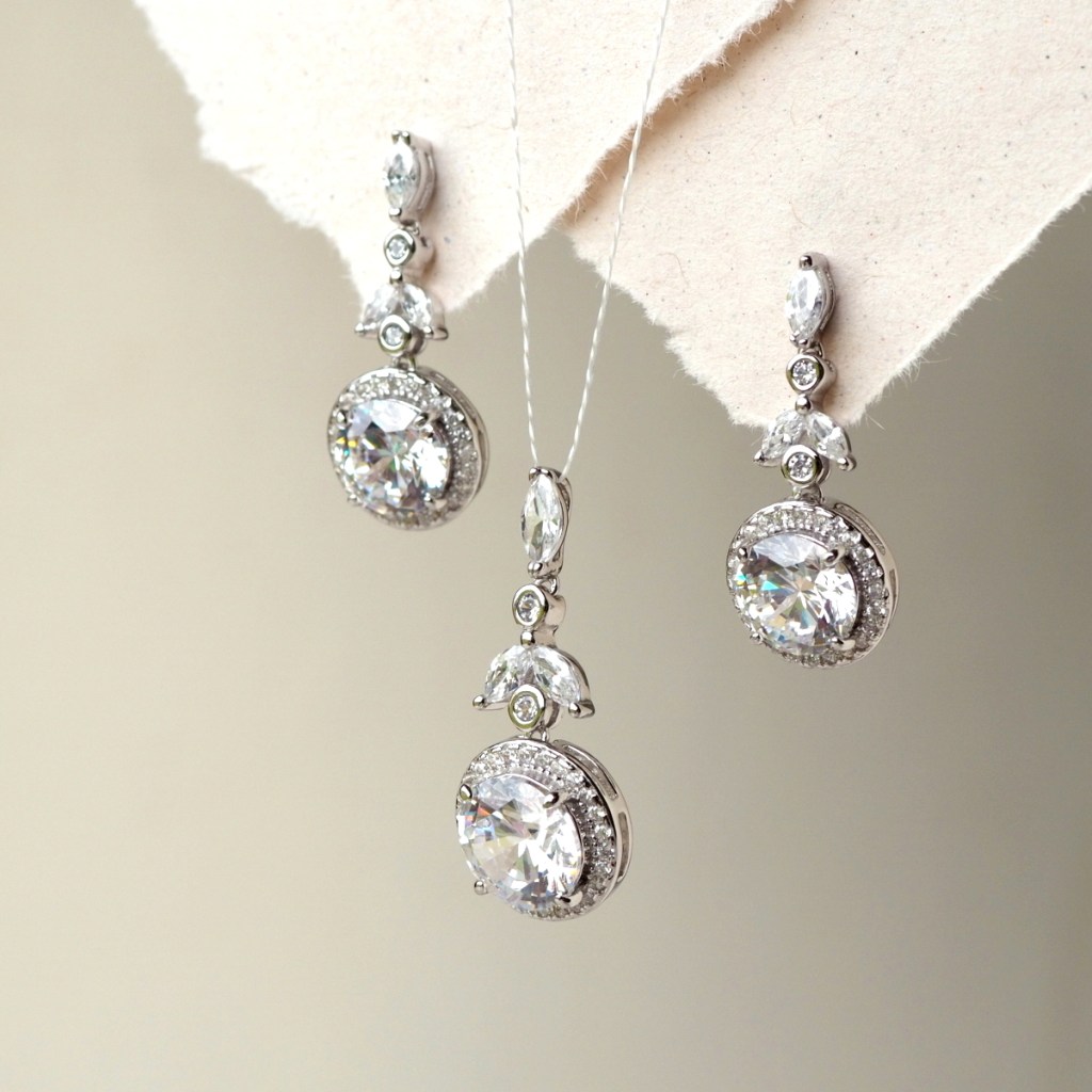 Elegant silver jewelry set featuring dangle earrings and a matching pendant, adorned with sparkling gemstones and intricate designs.