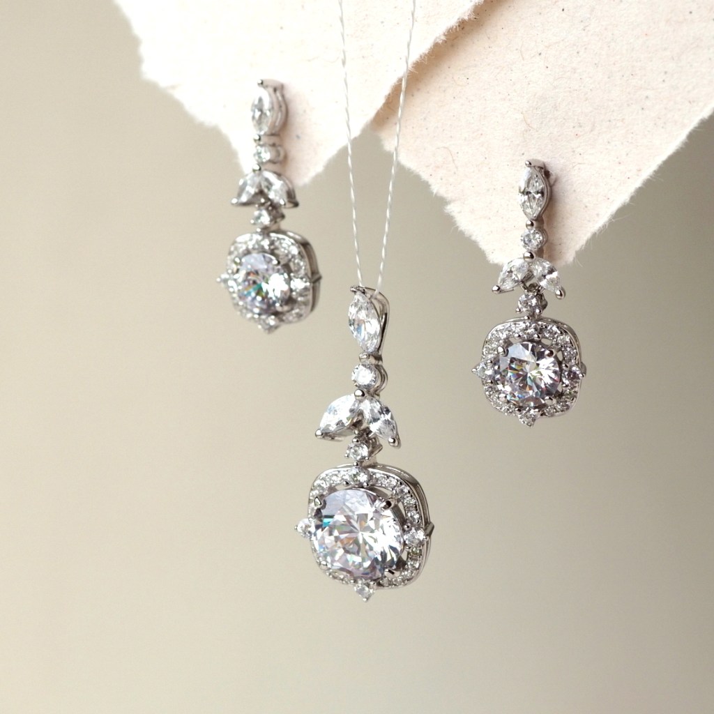 A set of elegant silver jewelry featuring a pendant and matching earrings, adorned with sparkling round and marquise-cut gemstones.