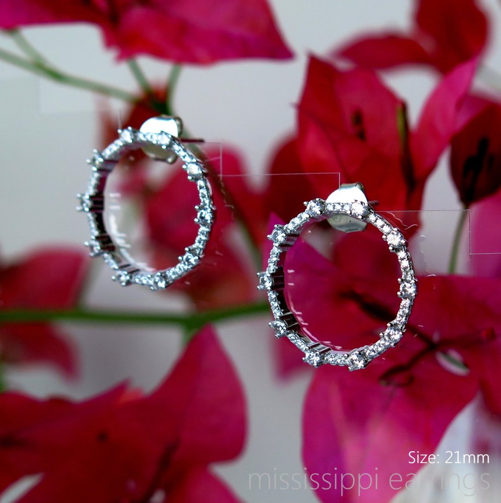 Silver hoop earrings adorned with crystals, displayed against a backdrop of pink bougainvillea flowers. Size: 21mm.