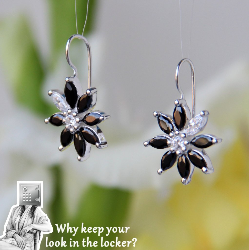 Close-up of elegant flower-shaped earrings featuring black and clear gemstones on silver hooks, with a blurred floral background.